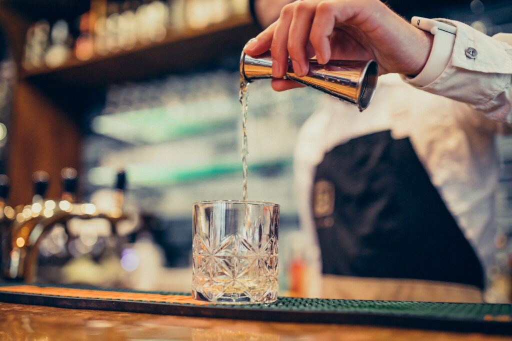 Bartender Hands Pouring Drink Into A Jigger To Prepare A Cocktail